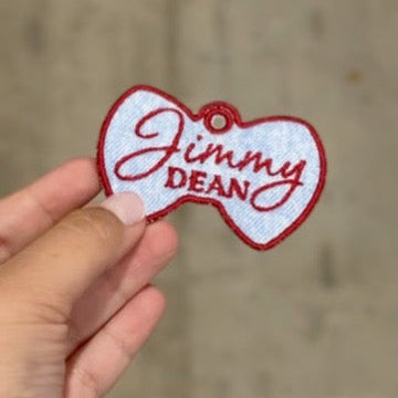 Bowtie-shaped 'Jimmy Dean' patch held by a hand against a concrete wall background