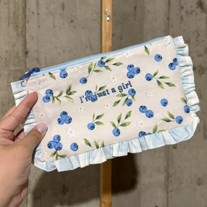 Hand holding a small pouch with floral design against a concrete wall.