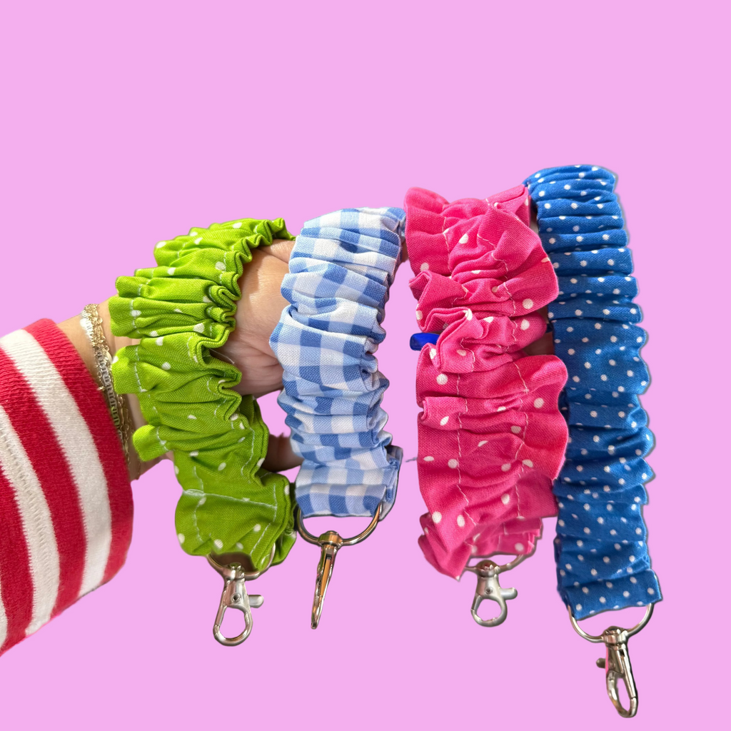 Four fabric scrunchie keychains in green, blue-and-white gingham, pink, and blue polka dot.