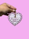 Heart-shaped 'Certified Yapper' tag held by a hand against a concrete wall.