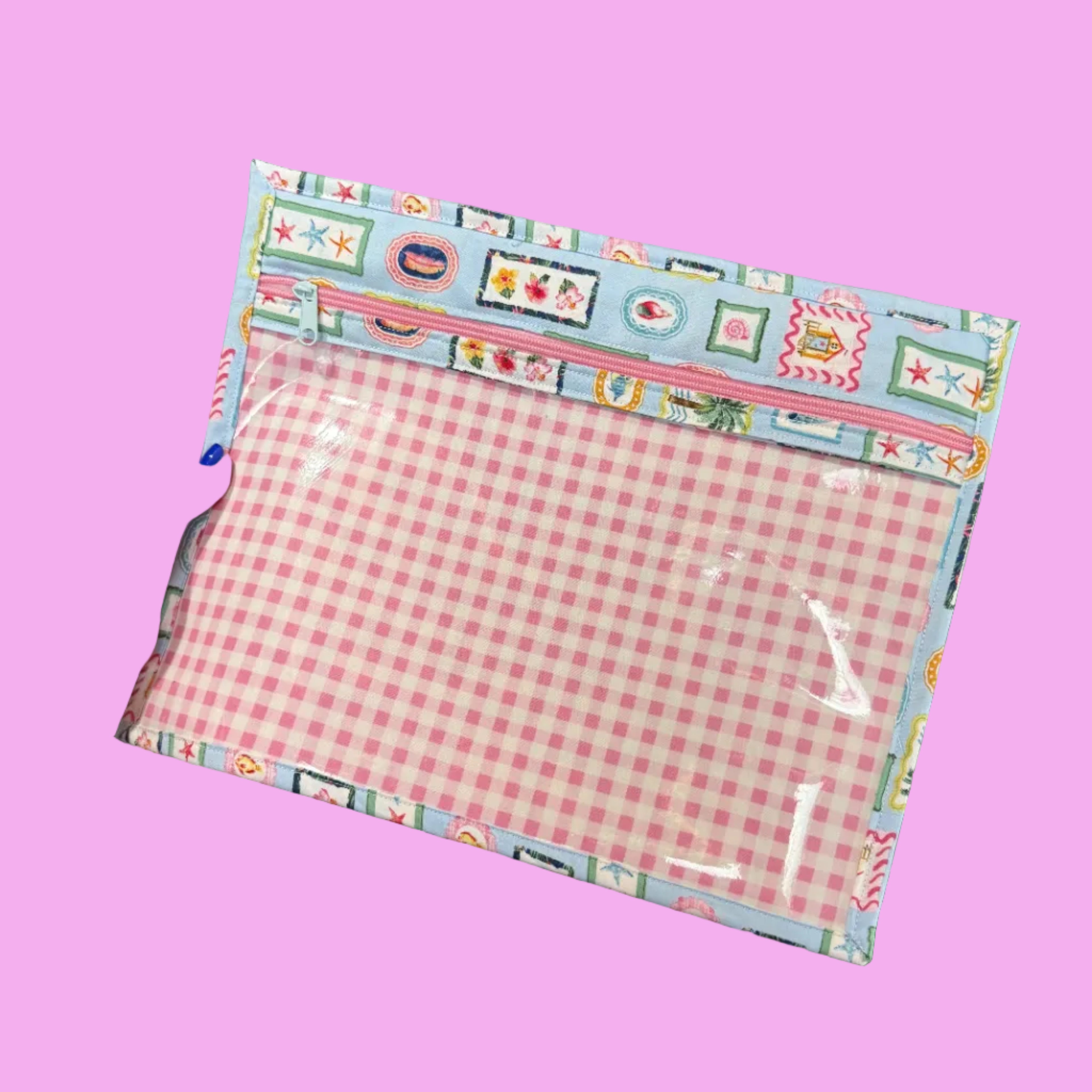 A hand holds a rectangular fabric pouch with a pink and white gingham patterned center and a colorful patchwork-style border.