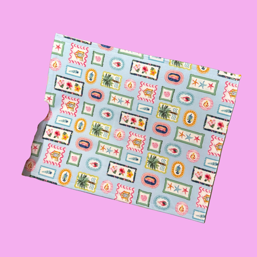 A hand holds a square piece of patterned fabric or paper with a colorful retro geometric design on a light blue background.