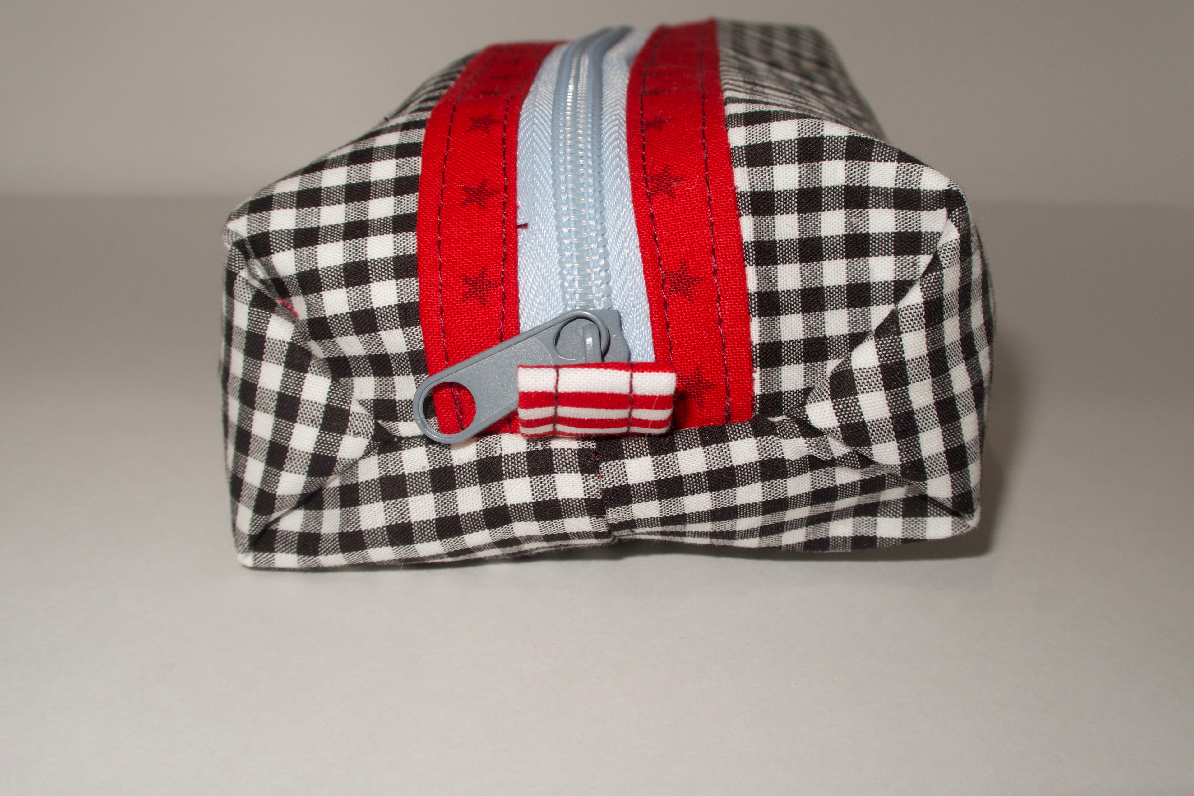 Black and white checkered pouch with red zipper on a gray background