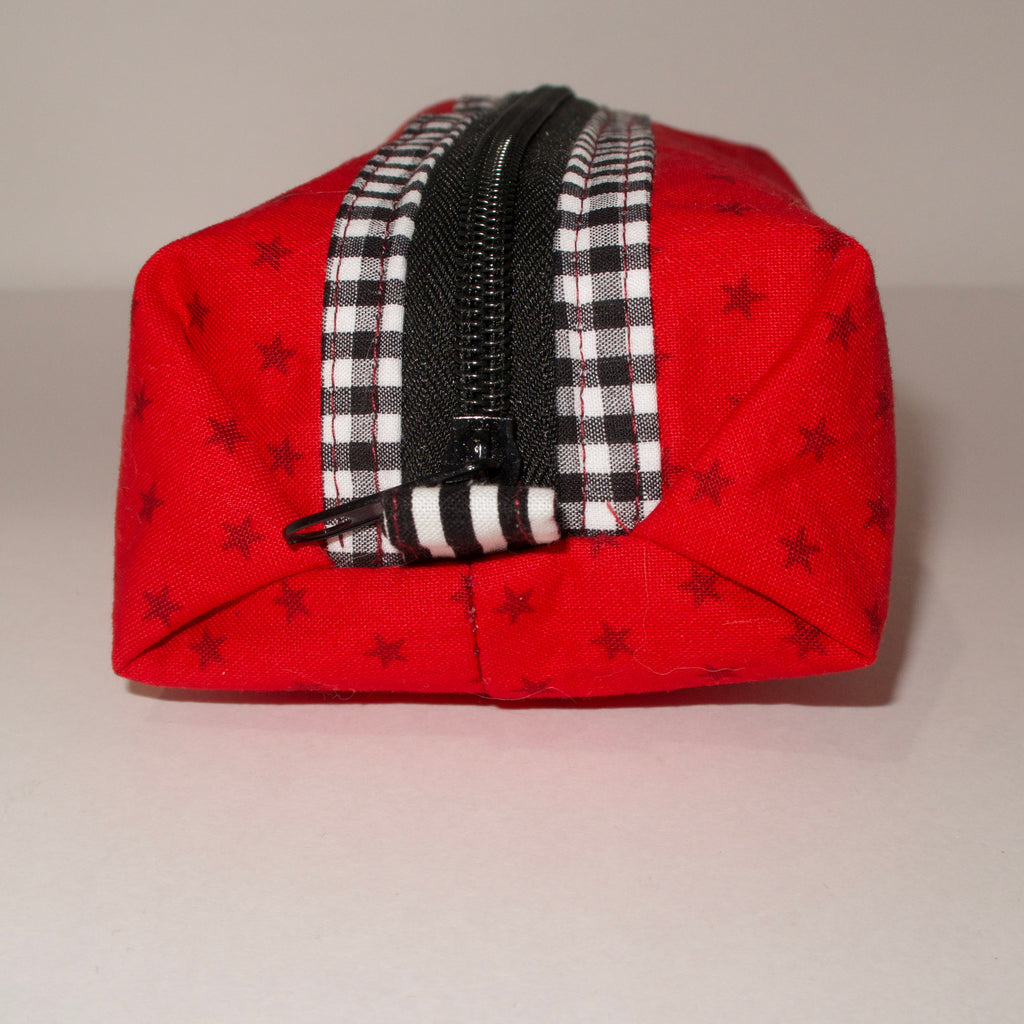 Red fabric pouch with black star patterns and a checkered zipper on a beige background