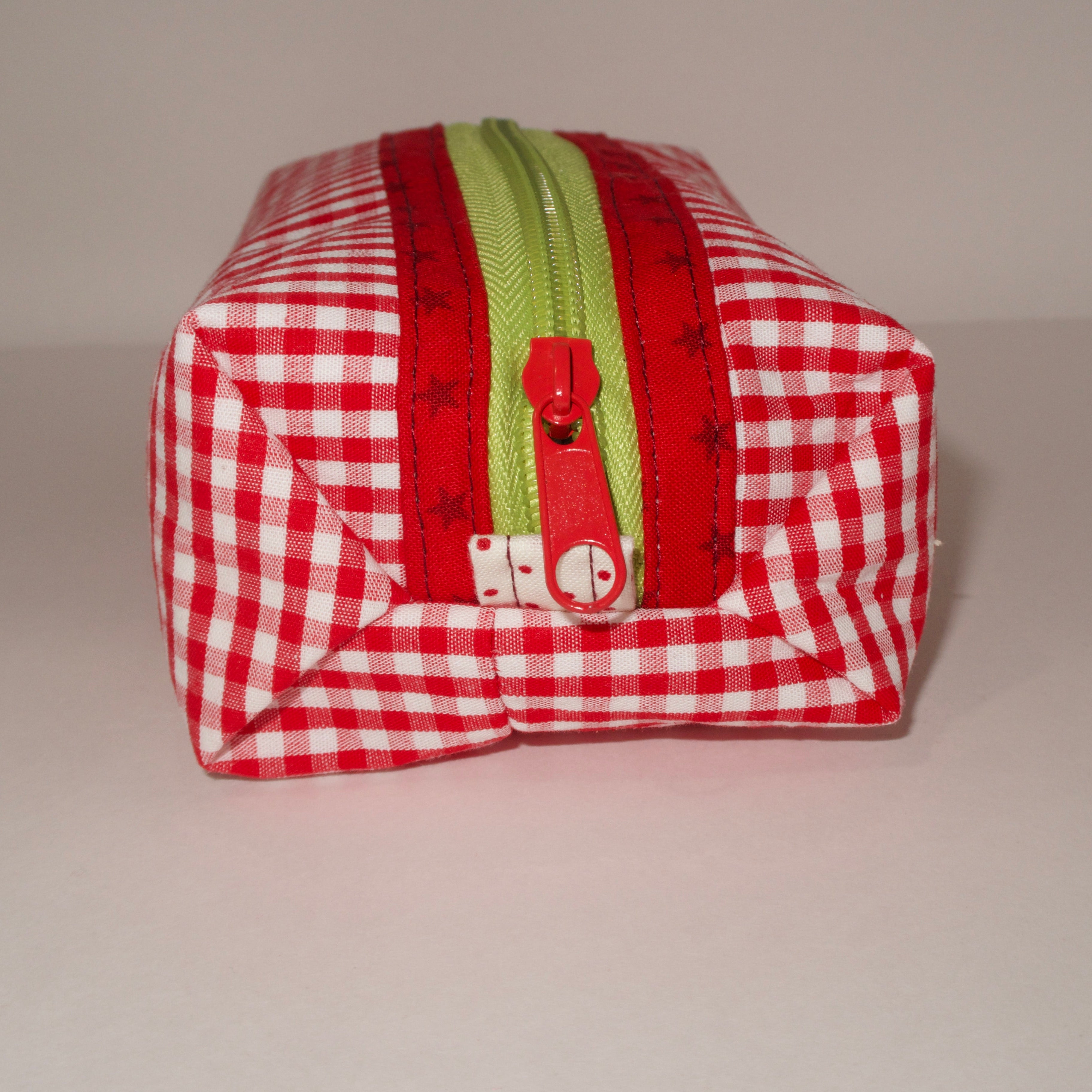 Red and white checkered pouch with a green zipper on a gray background