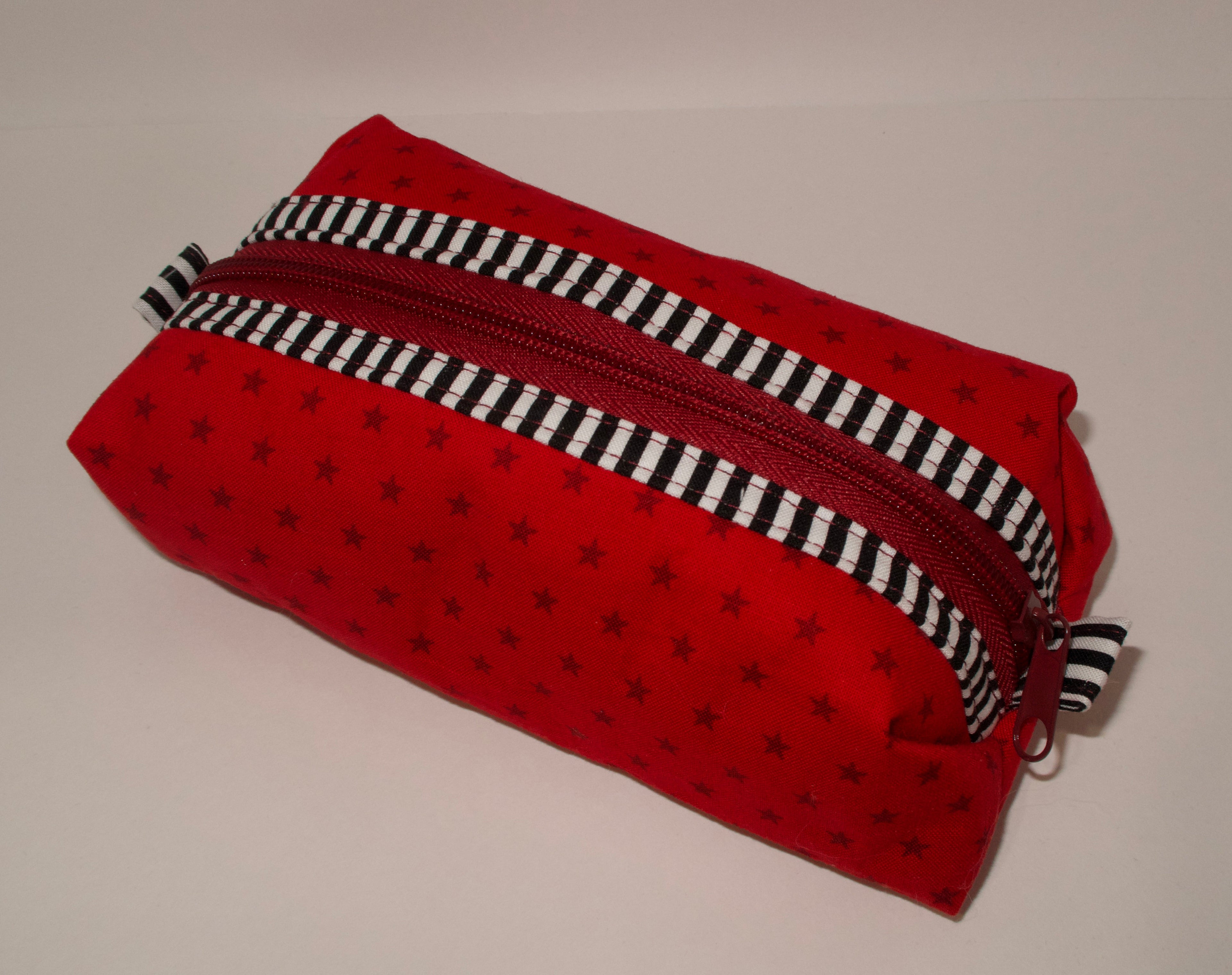 Red fabric pouch with black star pattern and a black and white striped zipper on a beige background