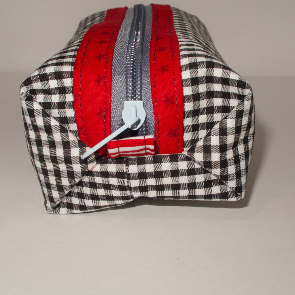 Black and white checkered fabric pouch with red and gray striped strap on a gray background