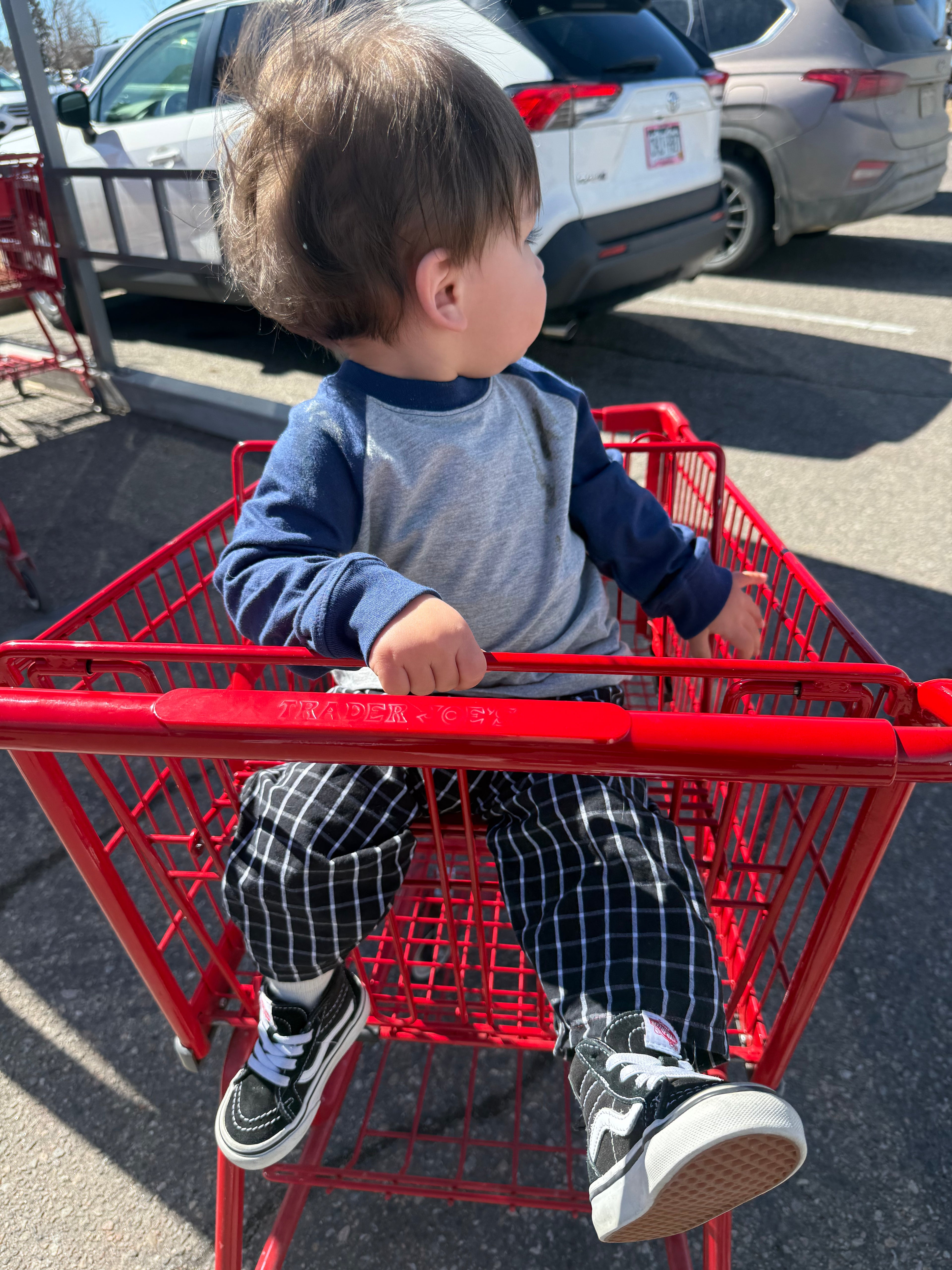 Child sitting in a red shopping cart in a parking lot.