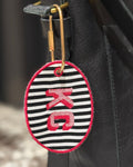 Black and white striped keychain with red letter 'K' on a black leather bag.