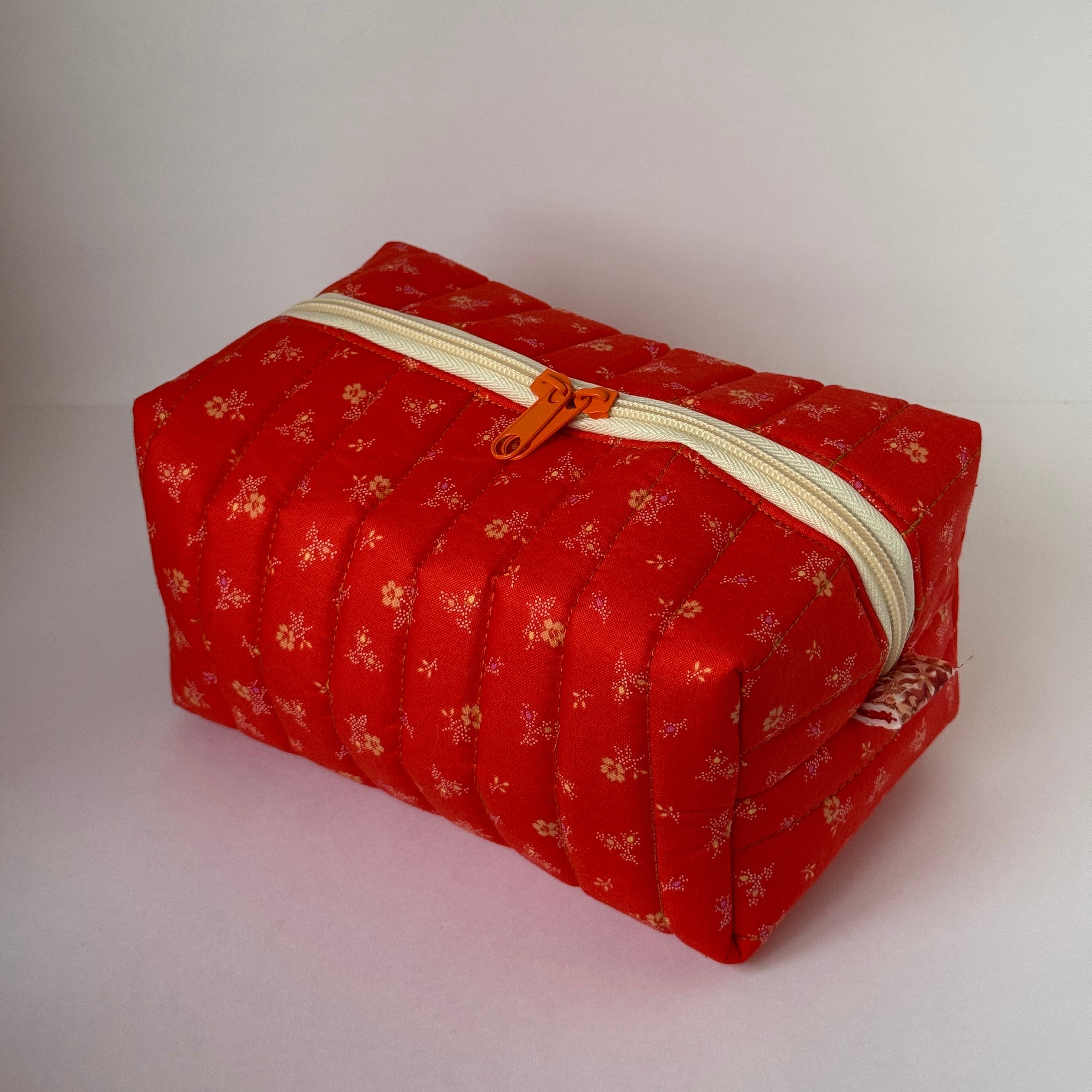 Red fabric pouch with gold patterns and a zipper on a light gray background