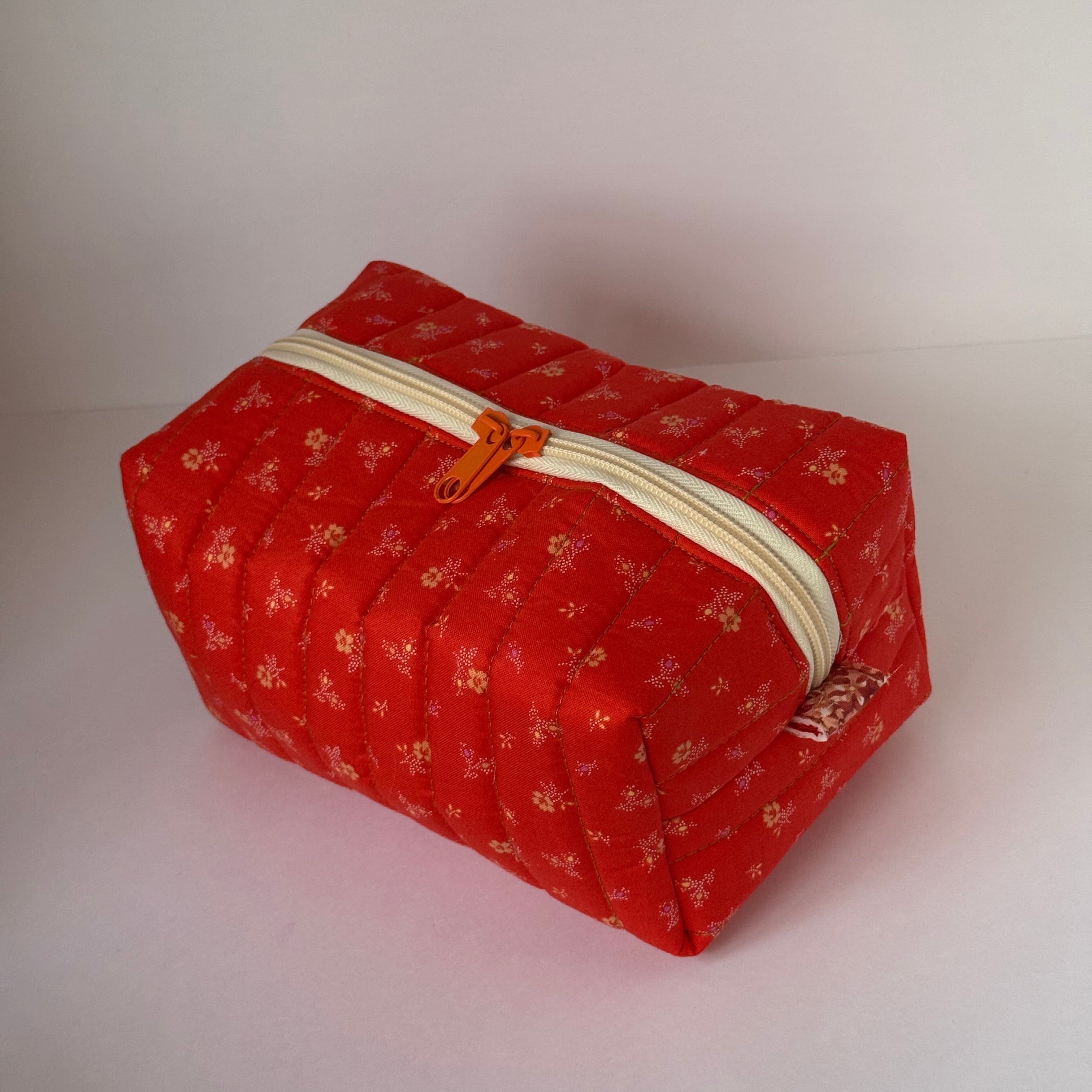 Red hexagonal pouch with floral pattern and zipper on a light pink background